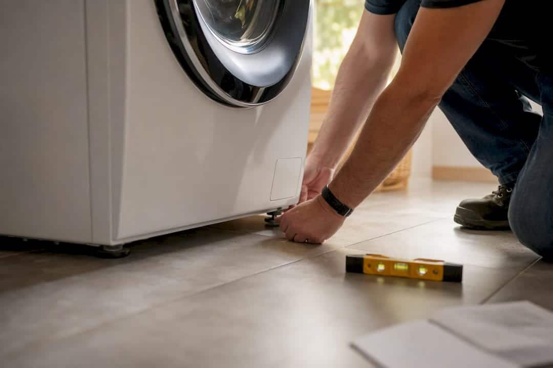 Hands leveling washing machine feet on floor