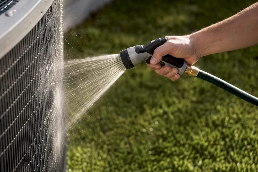 Homeowner rinsing an AC condenser coil